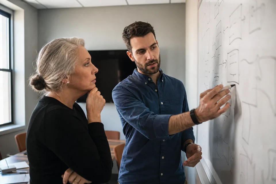 Compliance manager and security architect comparing options on a whiteboard in a meeting room