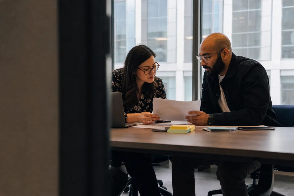Finance systems manager and security engineer comparing vendor notes at a conference table